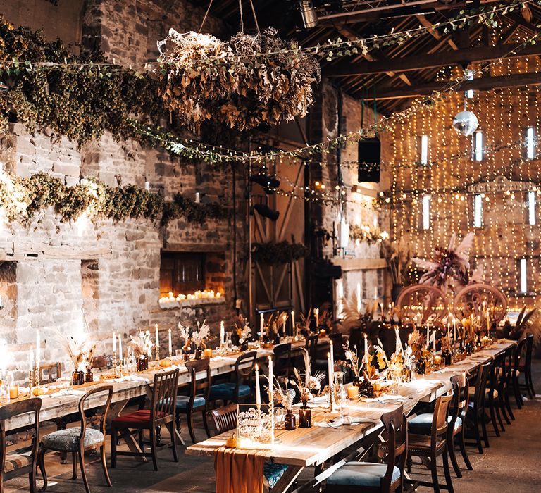 Large dried floral installations hang above barn reception with disco ball decor and wooden banquet tables with burnt orange colour scheme