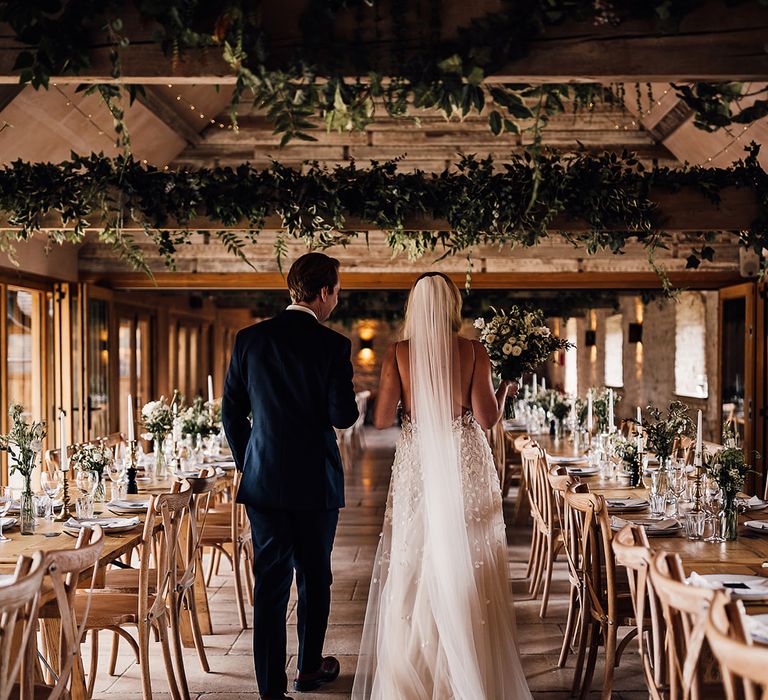 Bride and groom walk into Old Gore Barn for their wedding reception decorated in a classic style with a white and green tablescape 