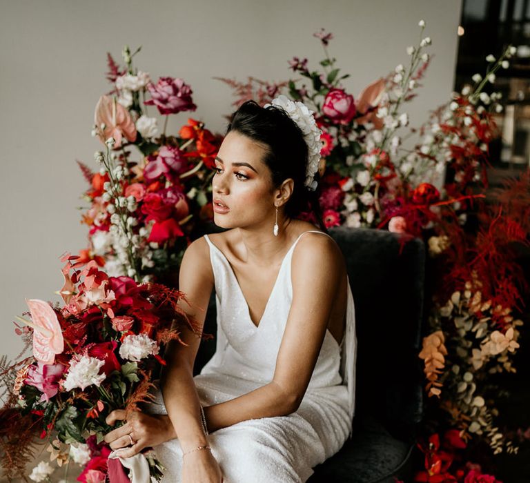 Bride in shimmery wedding dress and pink boots holding a bouquet in front of pink and magenta wedding flowers 