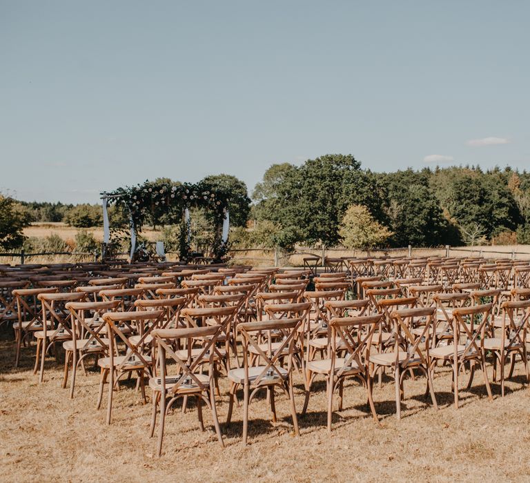 Outdoor wedding ceremony at High Billinghurst Farm with rustic wooden chairs and floral pergola 