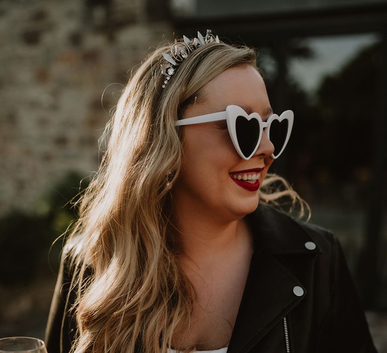 Bride in corset look satin wedding dress and white heart sunglasses with black leather jacket and bridal tiara 