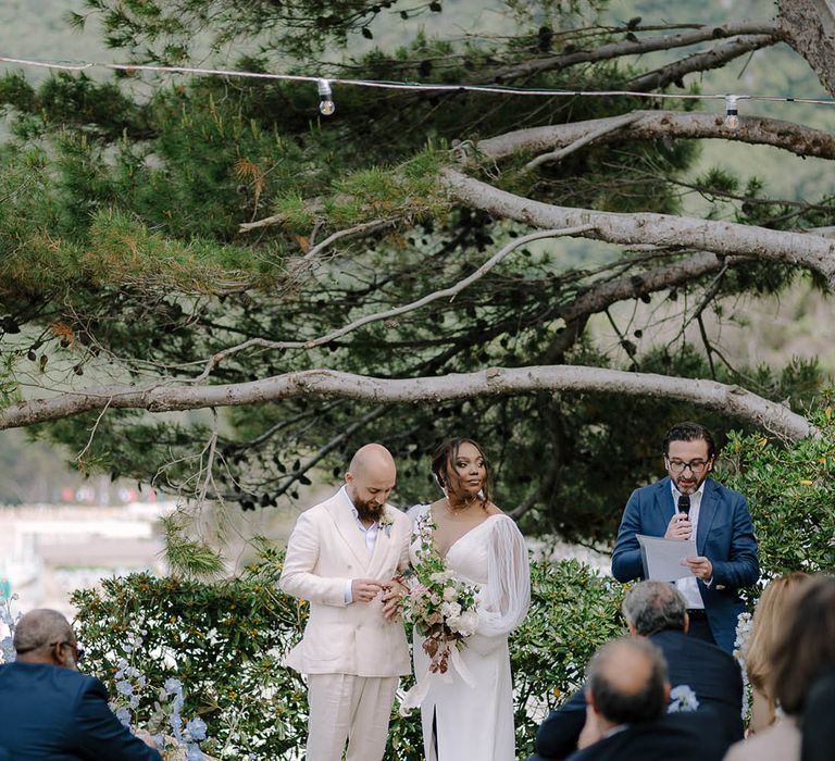 Bride and Groom stand at the alter in front of string lights and trees