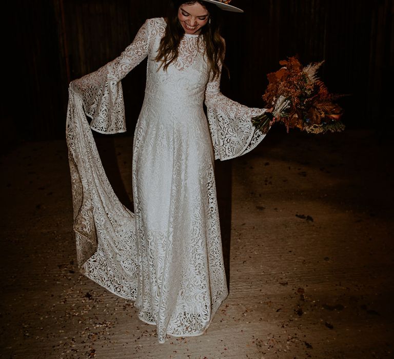 Bride with a laser cut lace wedding dress with bell sleeves and a chic wedding hat with died flowers 