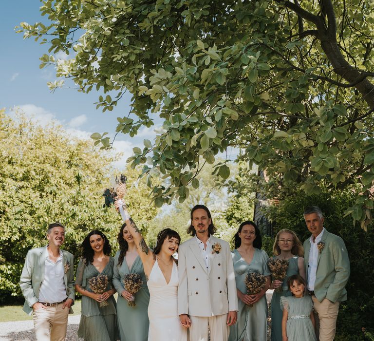 Wedding party in mismatched bridesmaid dresses and relaxed, casual suits with chinos and sage green blazers