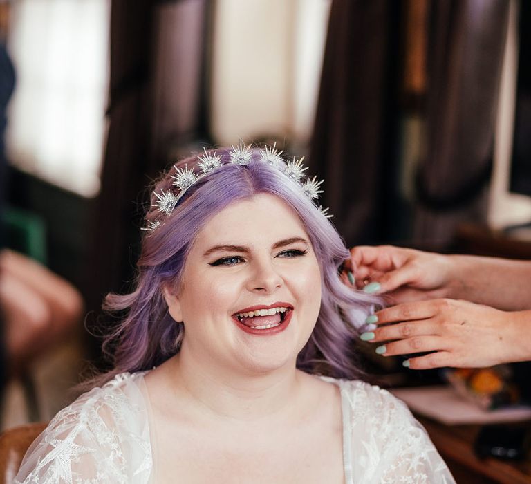 Bride in cowl neck satin dress with sheer star embroidered bridal robe wearing silver sparkly celestial headband, getting her bridal hair done 