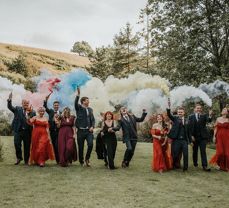 Wedding party in dark and burnt orange wedding outfits doing colourful smoke bomb photoshoot at Devon wedding venue 