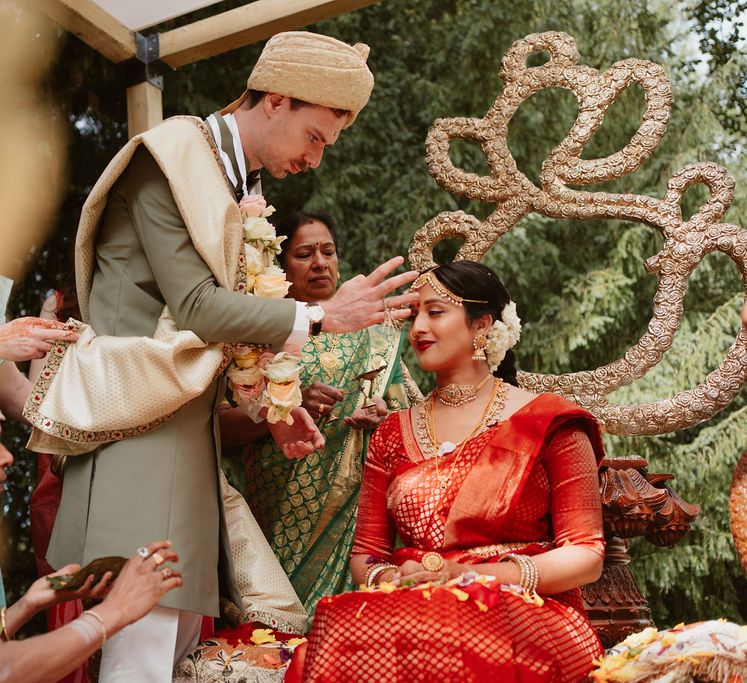 South asian bride in a red lehenga having paste put on her head during the Hindu wedding ceremony 