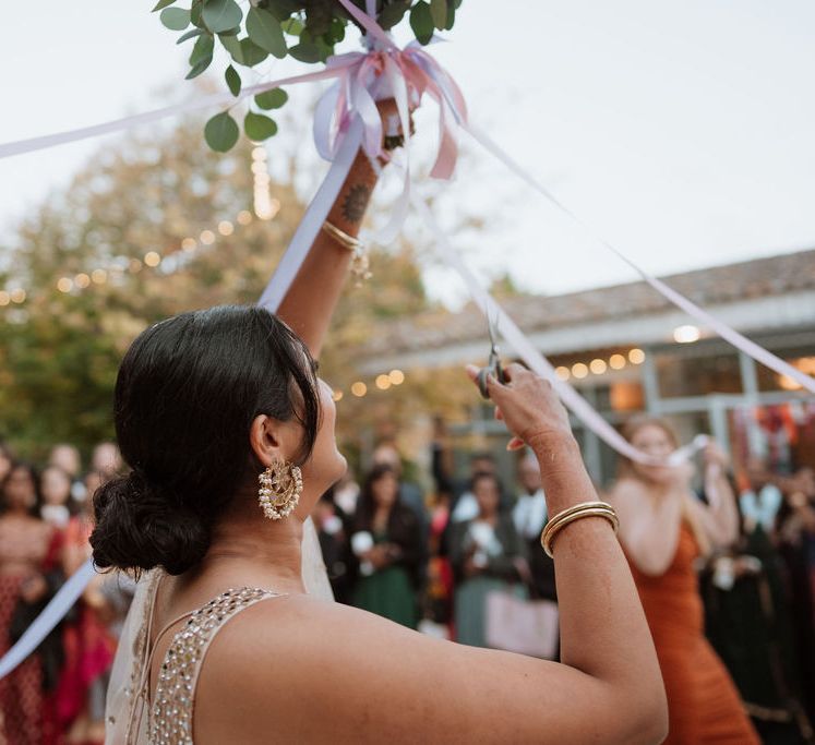 Bride cutting the ribbon attached to the wedding bouquet 