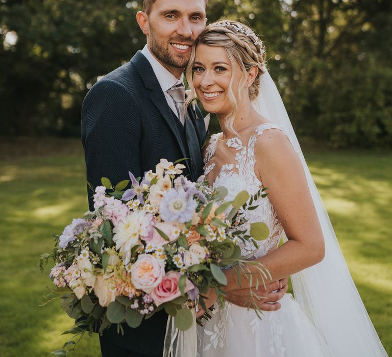 Bride in illusion lace wedding dress holding pretty pastel wedding bouquet with the groom in a dark suit for the Dove Barn in Suffolk wedding 