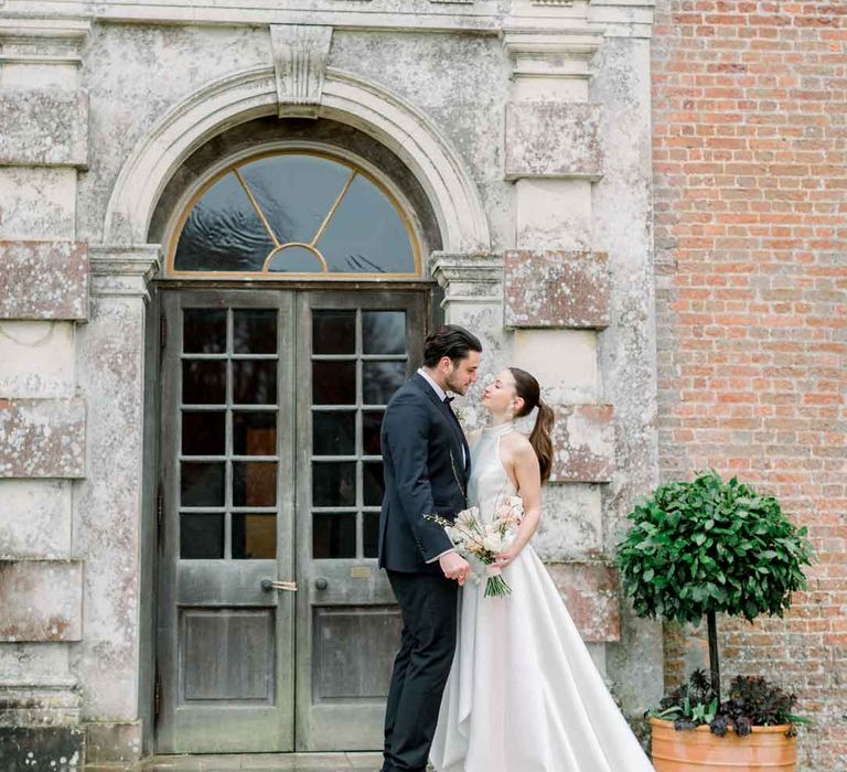 Bride in satin look halterneck wedding dress embracing groom in black tuxedo with black bowtie 