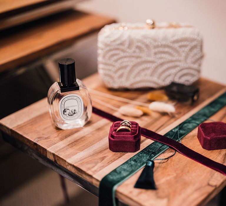 Wedding perfume laid out with the pearl clutch bag and red velvet ring box with gold wedding bands 