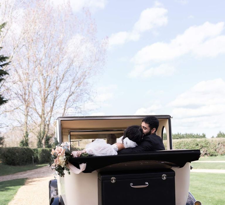 Classic vintage wedding car with the hood down and the bride and groom sharing a kiss 