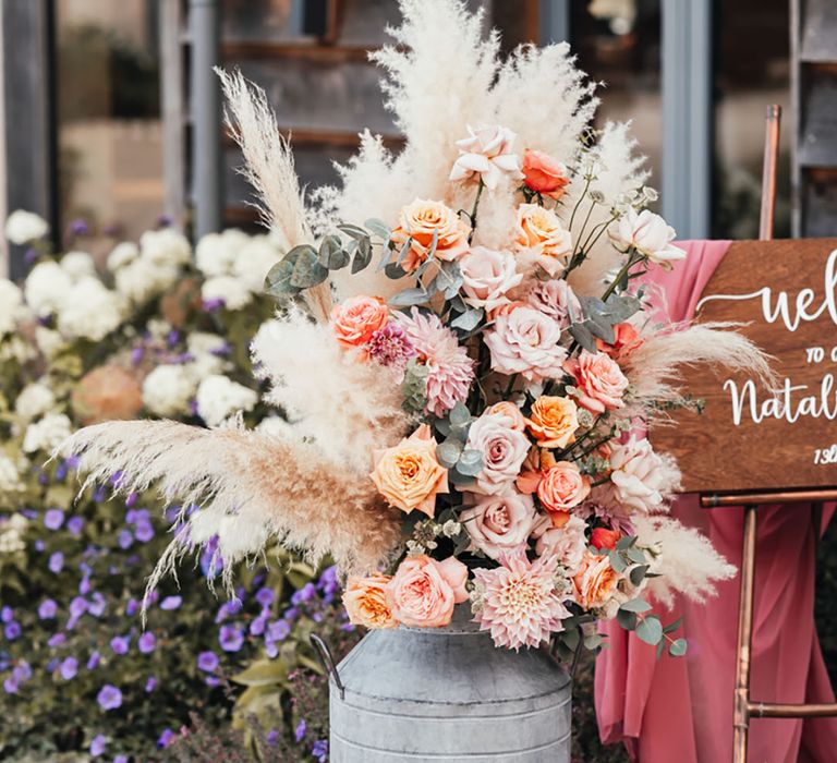 Vintage milk churn full of pink and orange roses with cafe au lait dahlias with pampas grass decor 