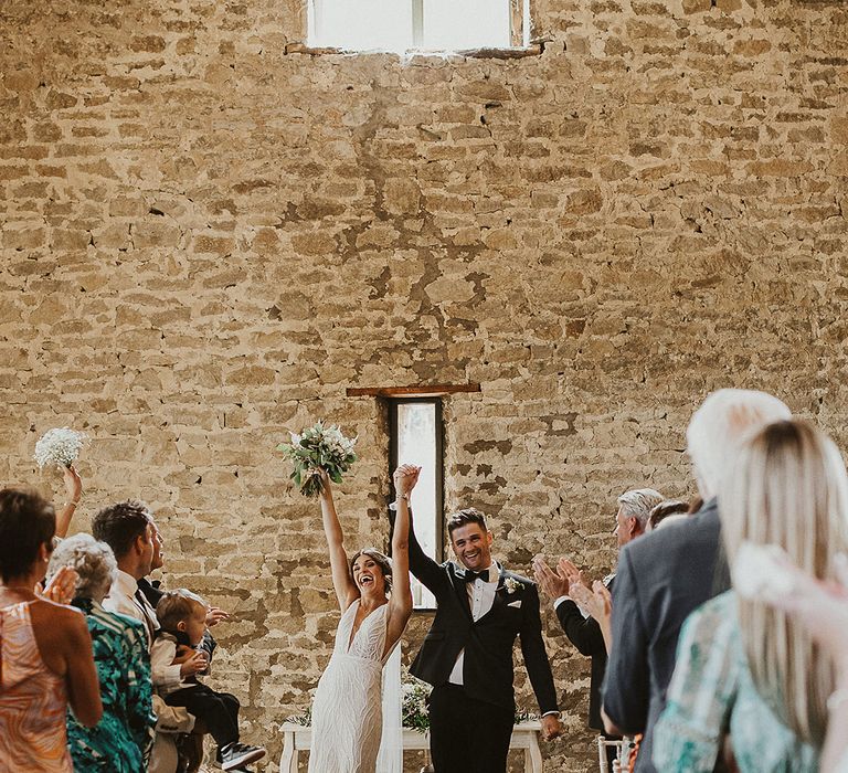 The bride and groom turn and face their guests as they raise their arms in celebration of being married 