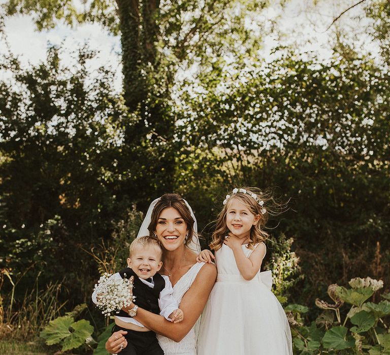 The bride smiling with the flower girl in a white dress and page boy in black tie for the rustic barn wedding 