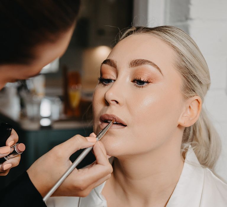 Bride sitting in white pyjamas as she gets her makeup done professionally for the wedding day 