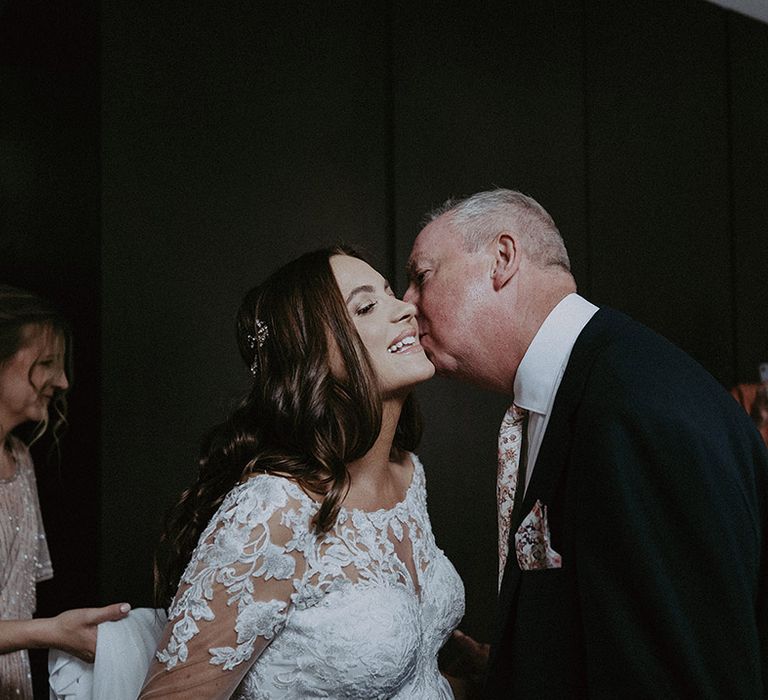 Bride in illusion lace wedding dress while being 7 months pregnant being kissed on the cheek by the father of the bride 