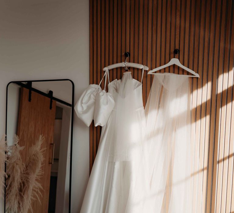 White silk wedding dress with bespoke sleeves hanging up in the getting ready room at Upton Barn wedidng venue