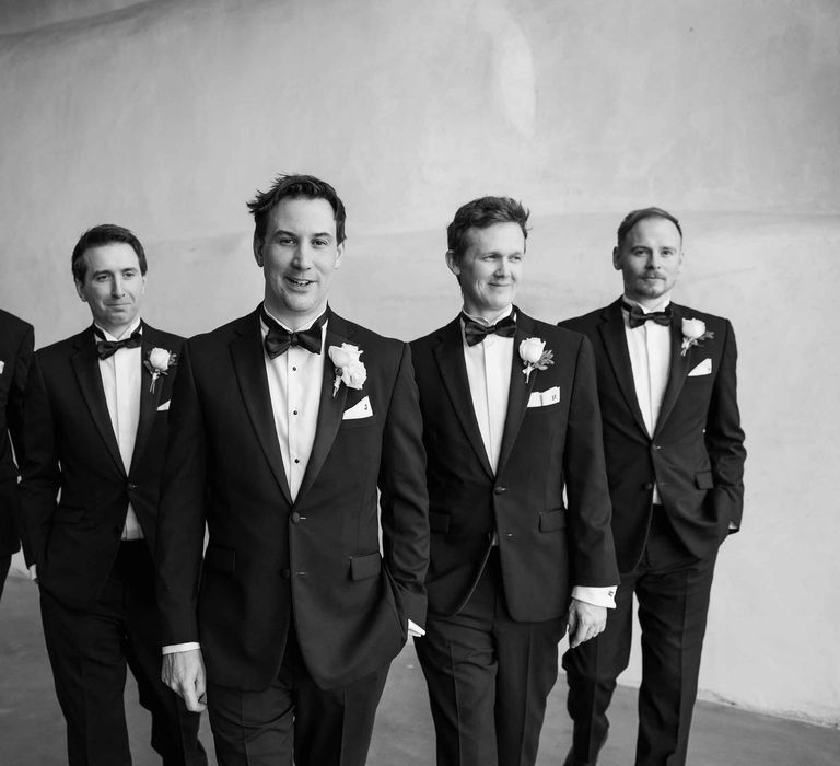 Black and white picture of groom and groomsmen lined up in black tuxedos and white rose boutonnière