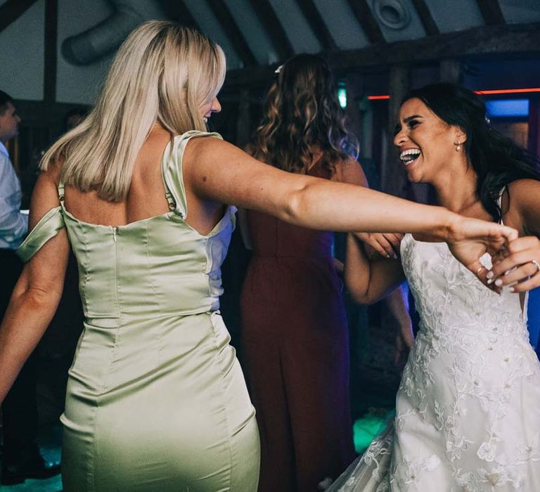 Bride in a-line tulle wedding dress with beaded lace applique with petals and a square neckline with side tulle cutouts dancing with wedding guest in sage green strappy dress at South Farm wedding