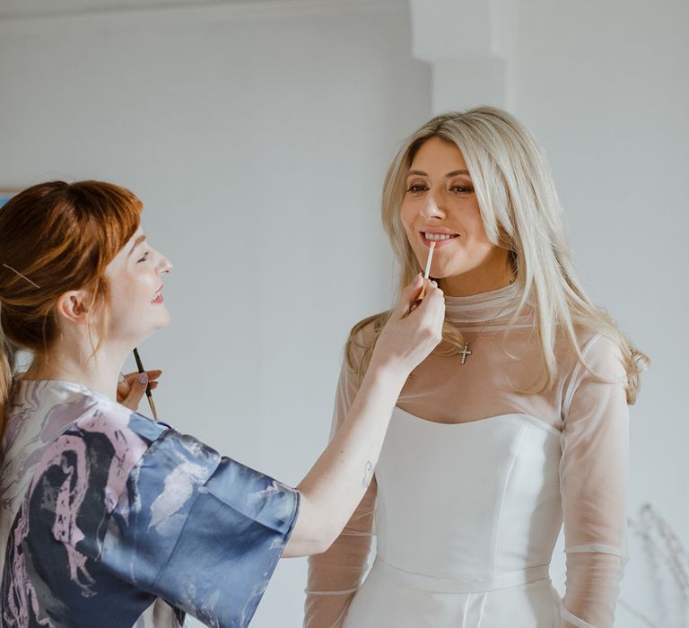 Bride in strapless wedding dress with mesh overlay top getting lipstick put on 