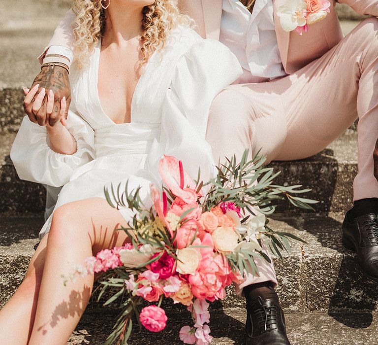 Bride holding pink wedding bouquet wearing funky heart shaped retro sunglasses with the groom 