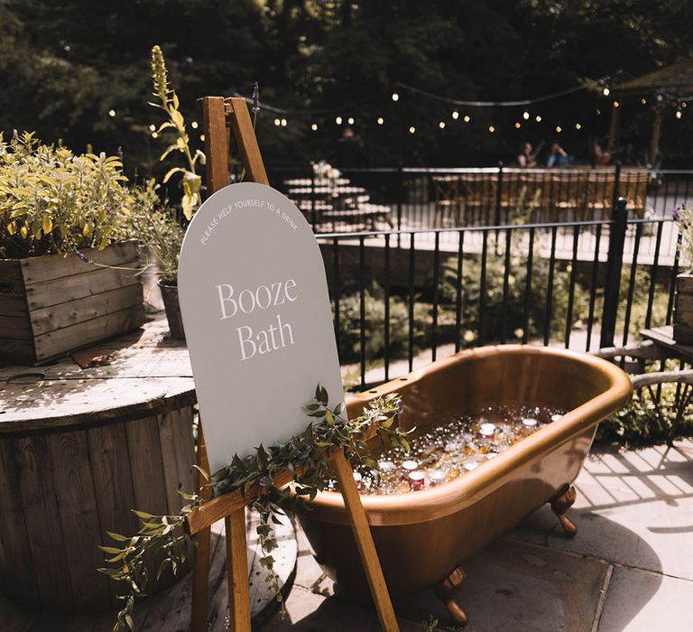 Booze bath wedding drinks station with neutral wedding signage on easel next to the bath 