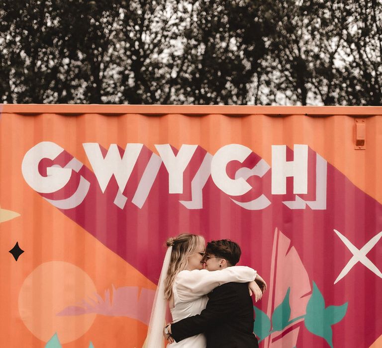 Bride in long sleeve wedding dress and bride in suit embrace each other at The Giraffe Shed wedding venue 