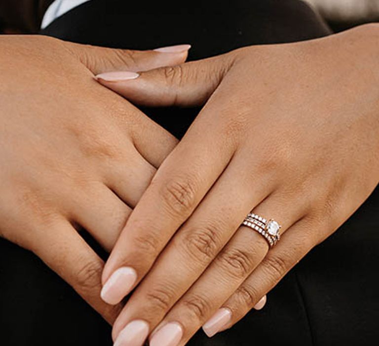 Bride embracing groom showing off round brilliant engagement ring and wedding band  How to find engagement ring size 