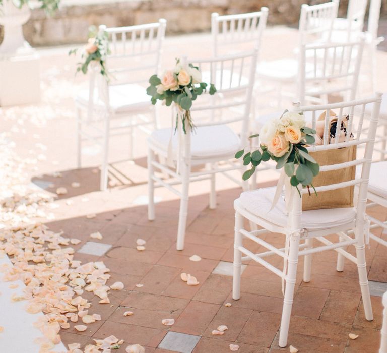 Peach roses attached to the corner of the chairs for aisle decor with peach petals lining the aisles 