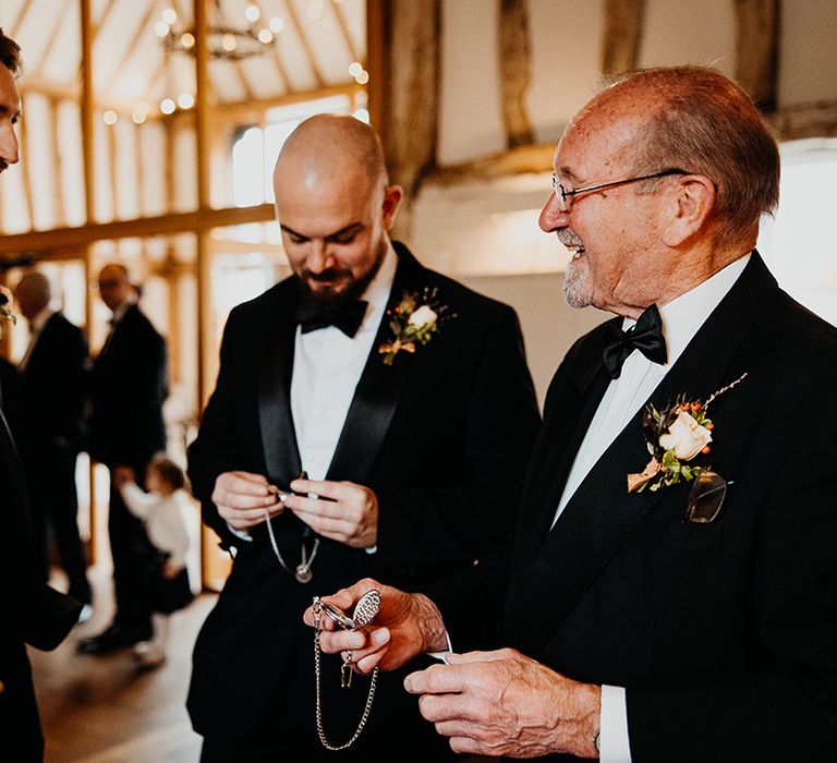 The groom and groomsmen stand together in matching black tuxedos 