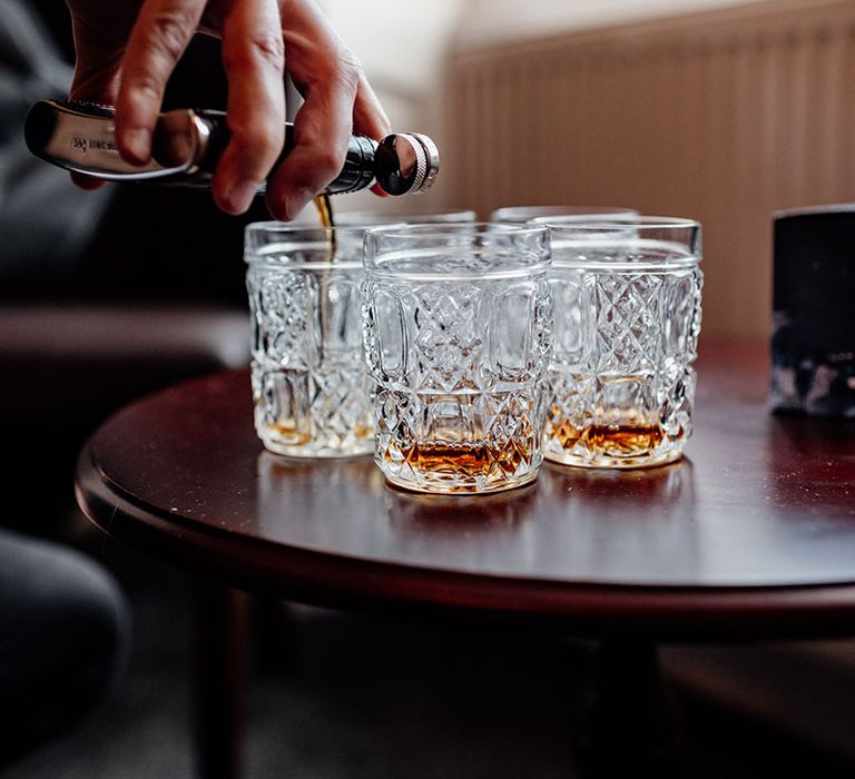 Groom and groomsmen pour whiskey into crystal tumblers as they all get ready for the morning of the wedding 