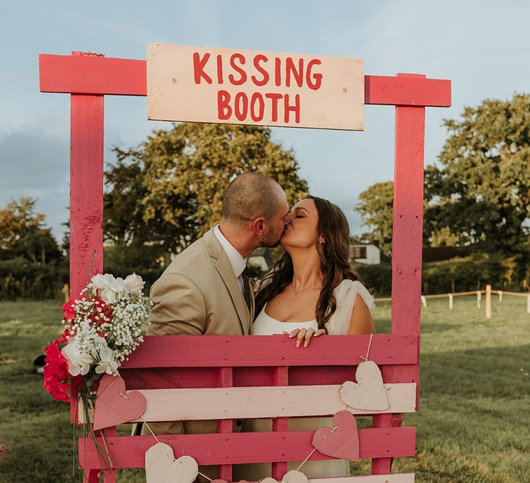 Bride and groom kissing in DIY kissing booth at their festival wedding with carnival games 