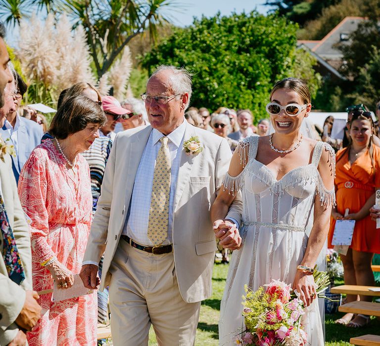 Father of the bride walking bride wearing corset sparkly wedding dress down the aisle at outdoor wedding 