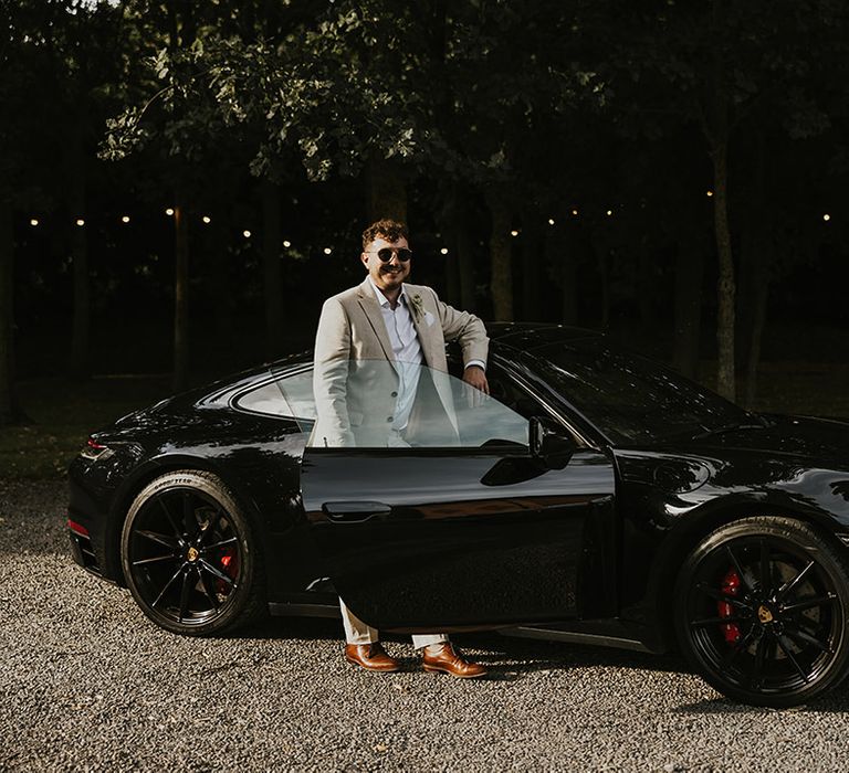 Black Porsche wedding car transport with groom in beige wedding suit 