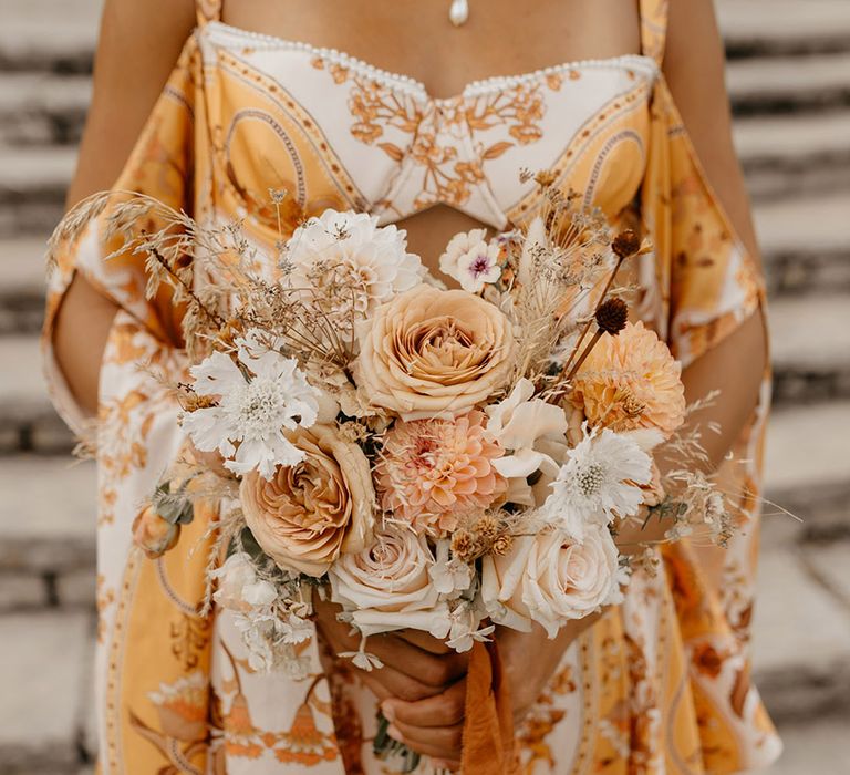 Bride in yellow and orange flower wedding dress with neutral tone wedding bouuqet with roses, dahlias and sweet peas 