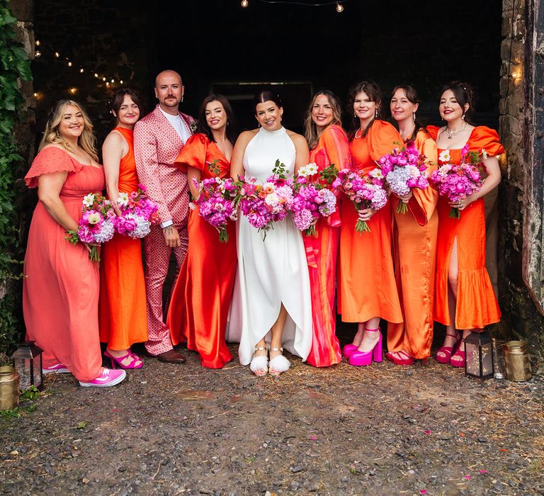 Bridal party with the bride for group photo wearing orange bridesmaid dresses and pink wedding shoes 