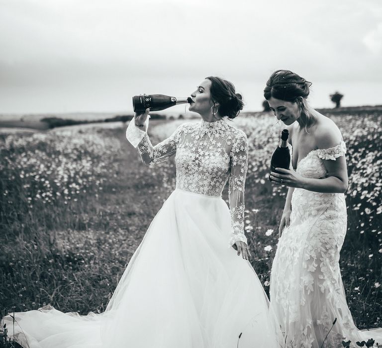 Two brides with flower patterned wedding dress drinking from the bottles of champagne as they celebrate their wedding day 