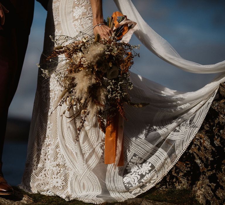 Boho bride holds pampas grass and gypsophila bouquet by a lake