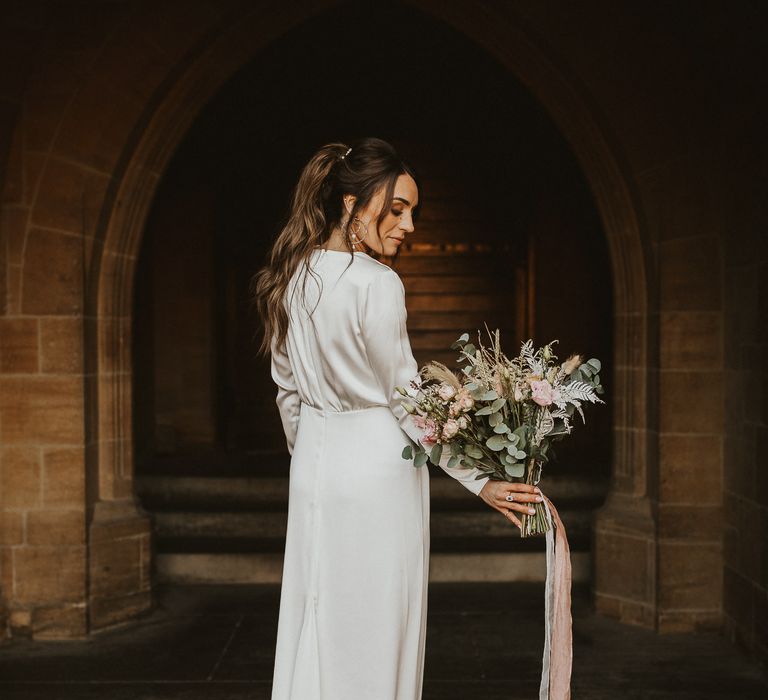 Bride stands with her back to the camera and shows pastel bouquet 