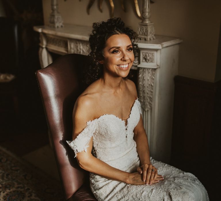 Bride in brown curly hair in an off the shoulder lace wedding dress on her wedding morning 