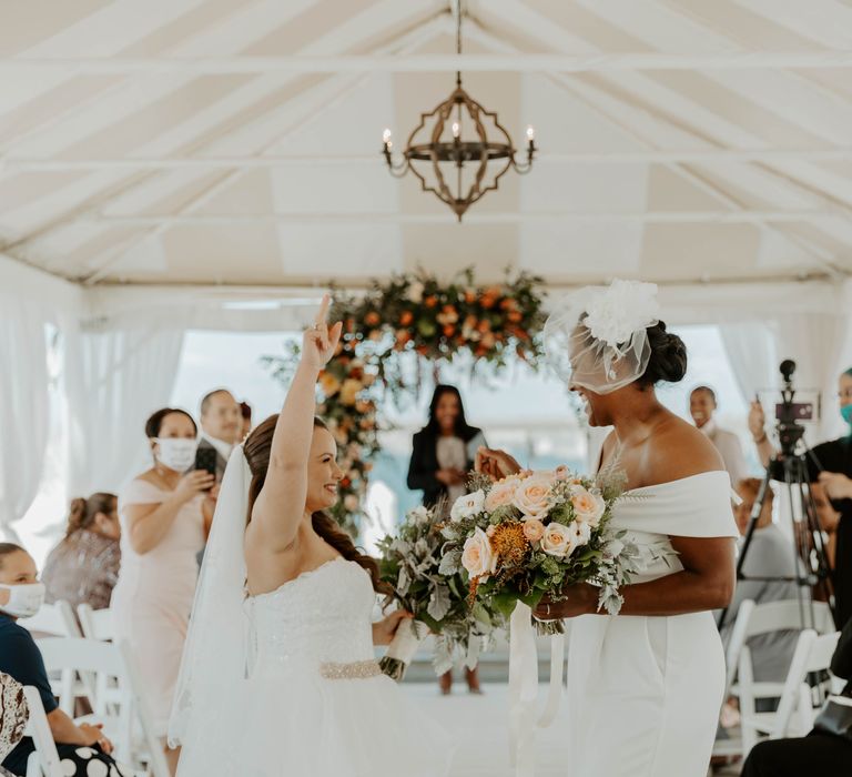 Two brides reaching the end of the aisle and high giving at their same sex wedding ceremony 