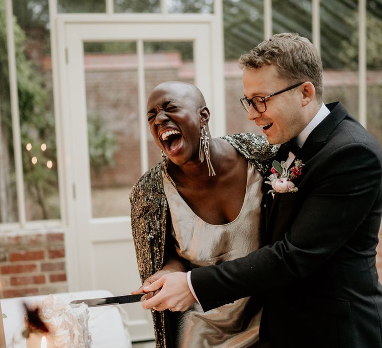 Bride and groom laughing whilst cutting their wedding cake at their intimate Our Beautiful Glasshouse elopement 