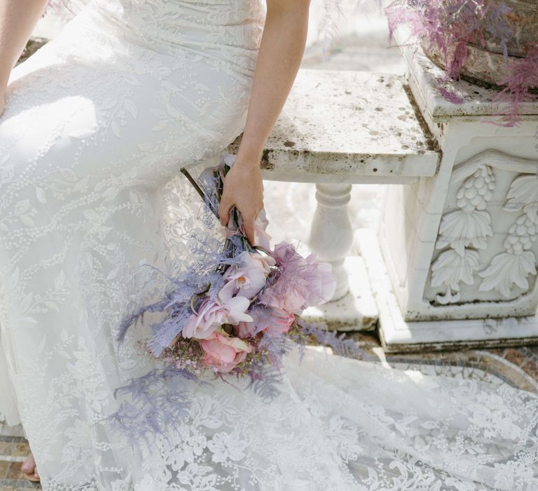 Pastel lilac floral bouquet next to lace gown