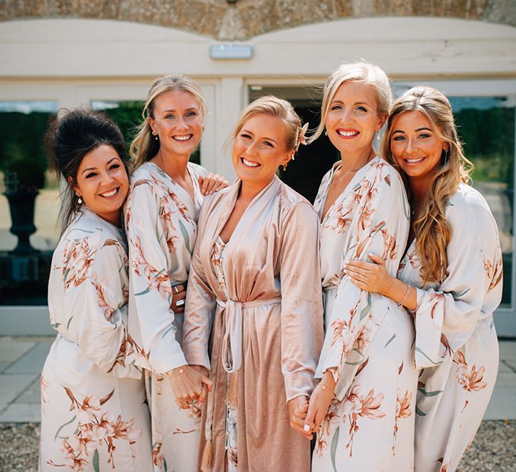 Bridal party wearing outside country barn with bride wearing peach wedding robe and bridesmaids wearing floral robes