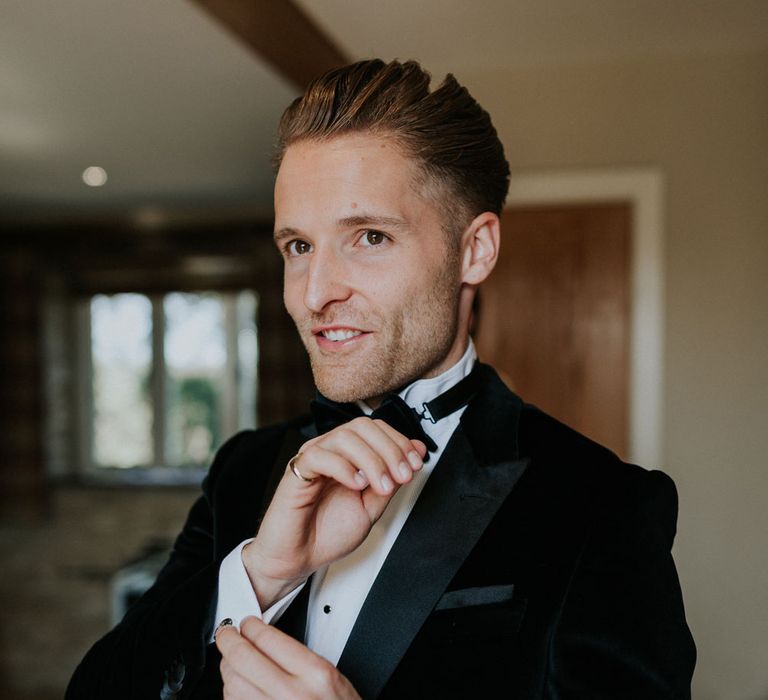 Groom in black velvet Hugo Boss suit, white shirt and black bow tie getting ready at Caswell House wedding