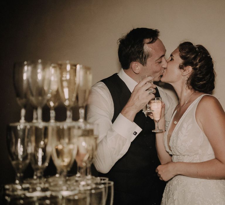 The bride and groom kiss with a glass of champagne