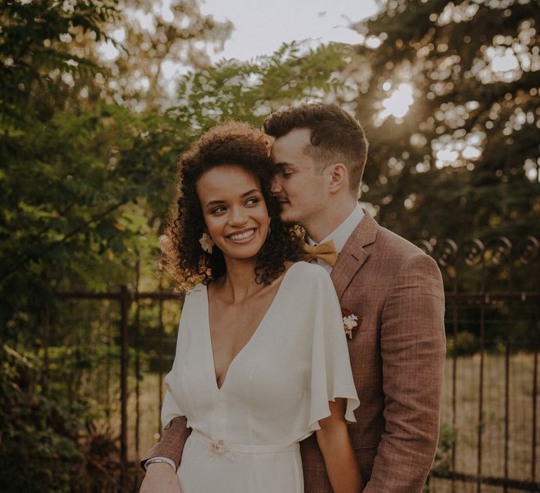 Groom in a brown wedding suit nuzzling his brides naturally curly hair 