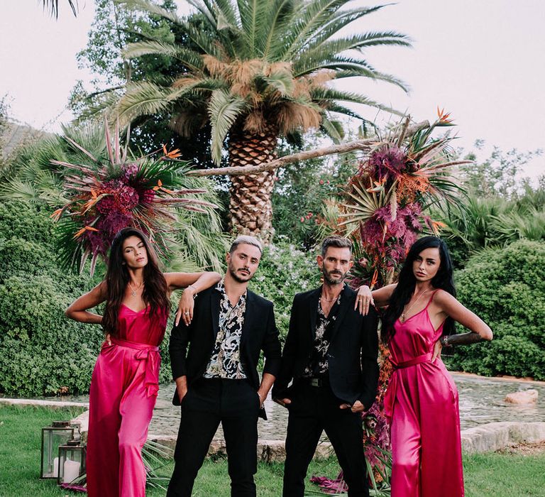 Drag race wedding inspiration with two groom sin black suits and two bridesmaid in bright pink jumpsuits. Photography by Stephanie Shenton.