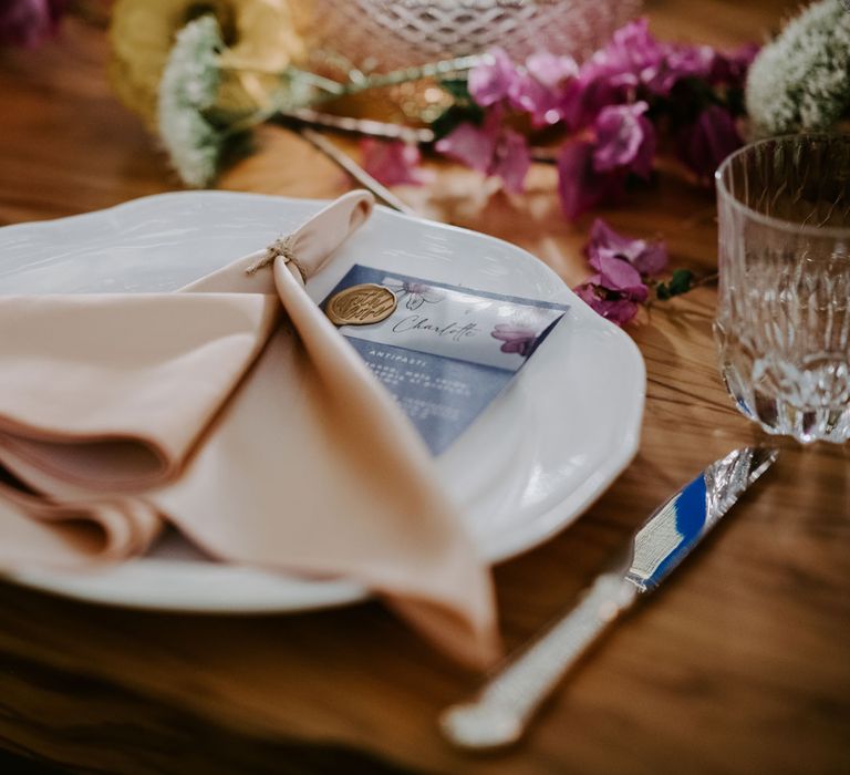 Light pink napkins on white plates next to cut crystal tumblers set on rustic wooden table at enchanted forest wedding in Italy